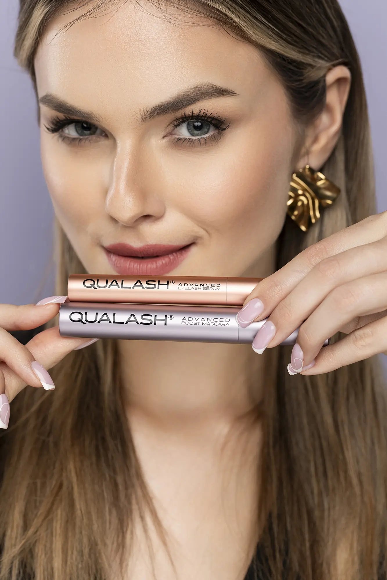 QUALASH Advanced Eyelash Serum과 Mascara Volume Max를 들고 있는 손 클로즈업