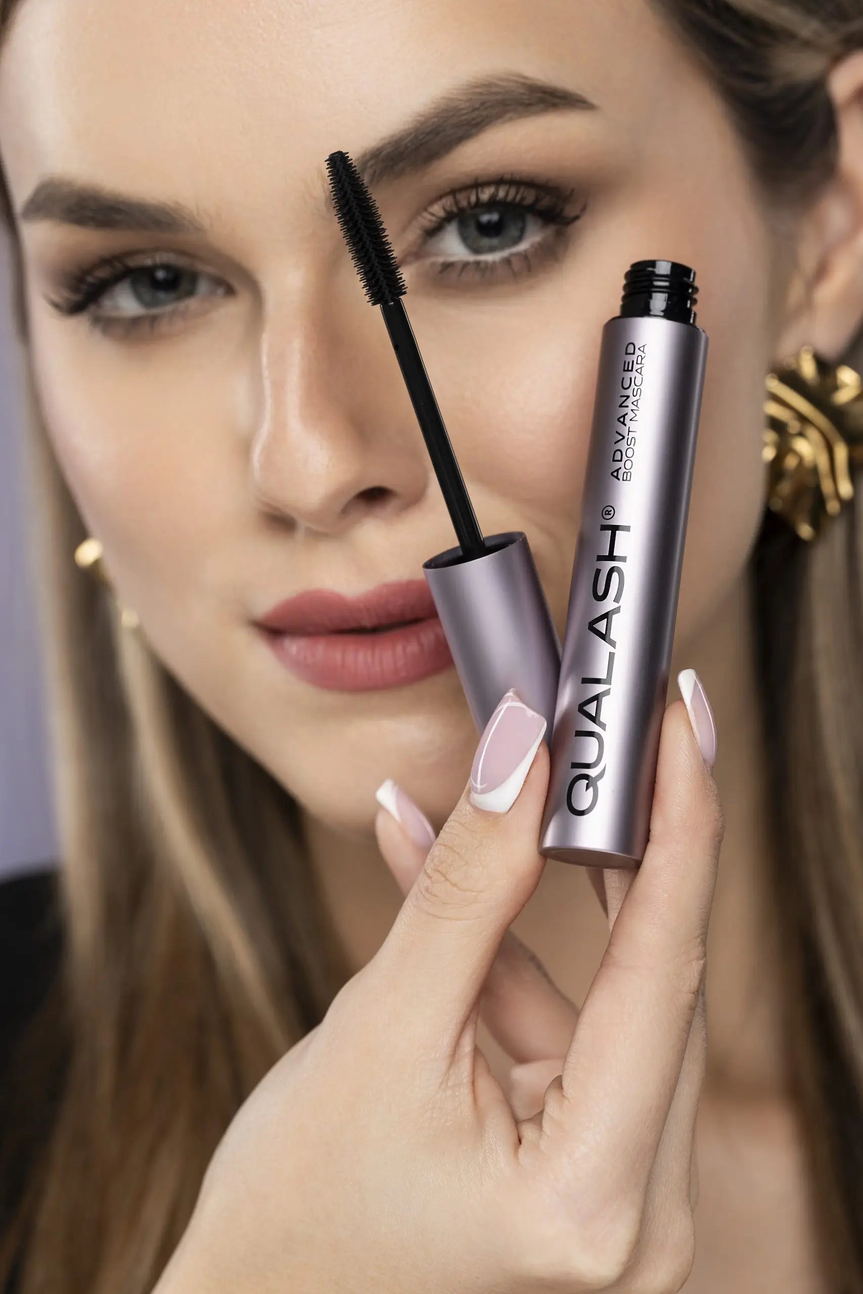 Grande plano de mulher a segurar QUALASH Advanced Volume Max, com a escova curva visível e pestanas volumosas