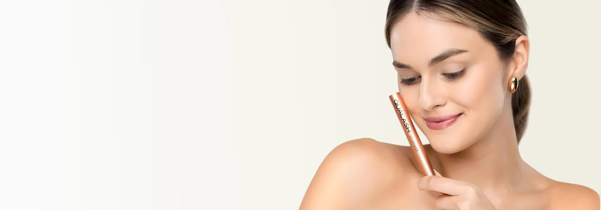 Beauty portrait of a woman holding Qualash lash mascara against a clean light background